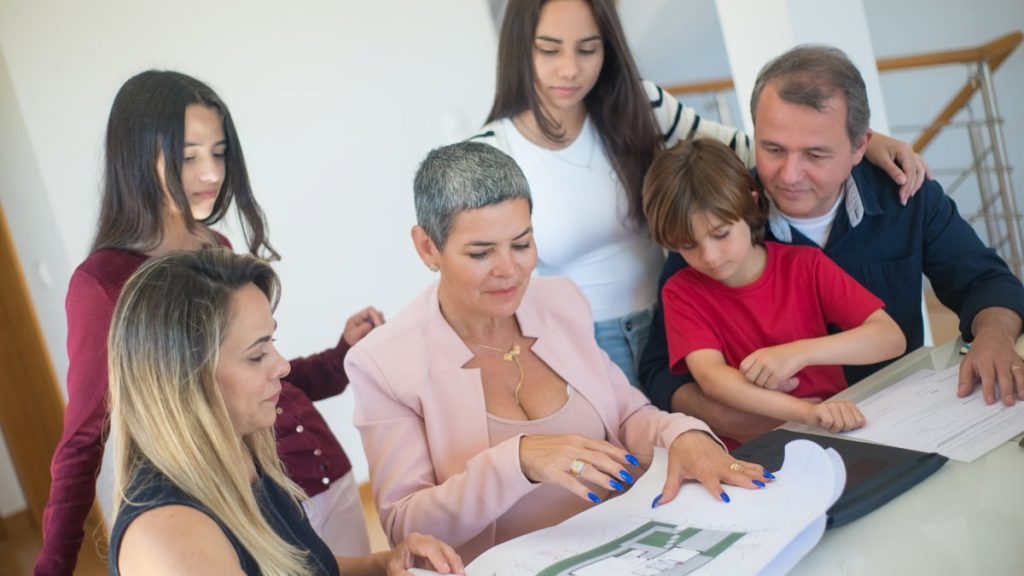 A family discusses property plans with a realtor indoors, focused on purchasing a new home.
