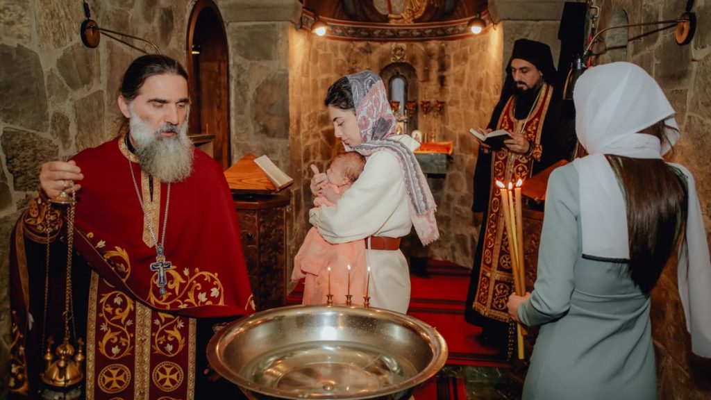 A sacred baptism ceremony inside an Orthodox church with priests and family.
