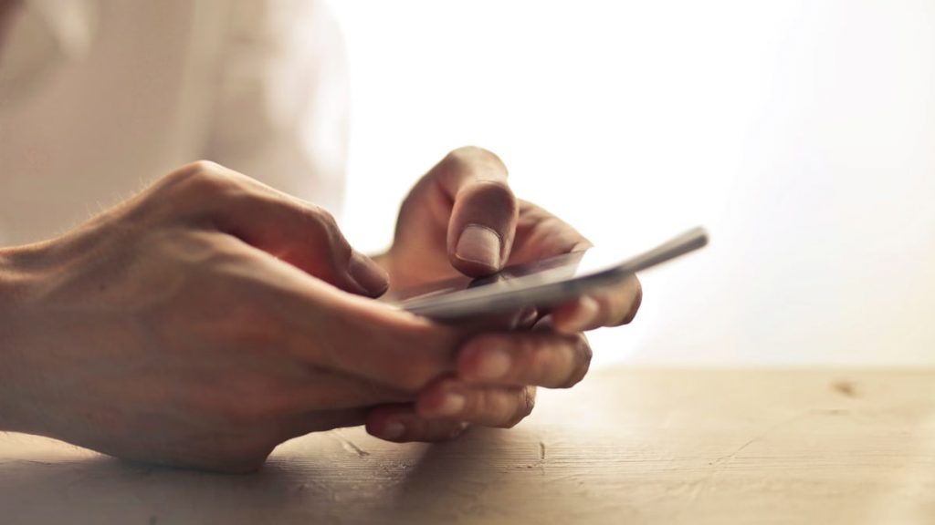 Close-up of an individual's hands holding a smartphone on a table indoors.